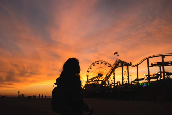 The silhouette of a young girl against a theme park at sunset.