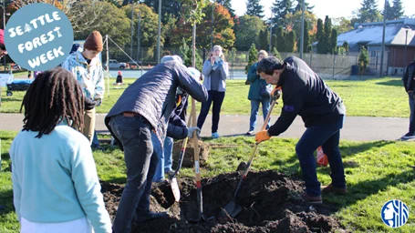  Photo of Mayor Bruce Harrell planting a tree with 2 community members in a Seattle Park. A couple of people are watching and taking photos. On the top left corner, a blue circle reads “Seattle Forest Week”. On the bottom right corner is the blue and white City of Seattle logo.  
