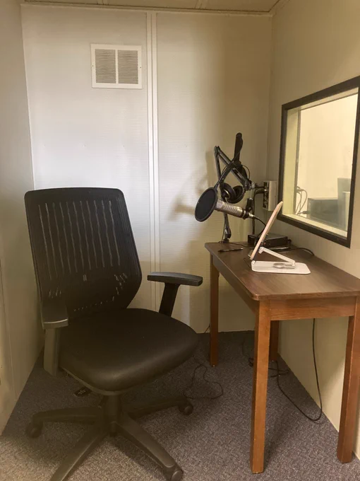 A desk chair positioned in front of a microphone and screen inside a recording booth.