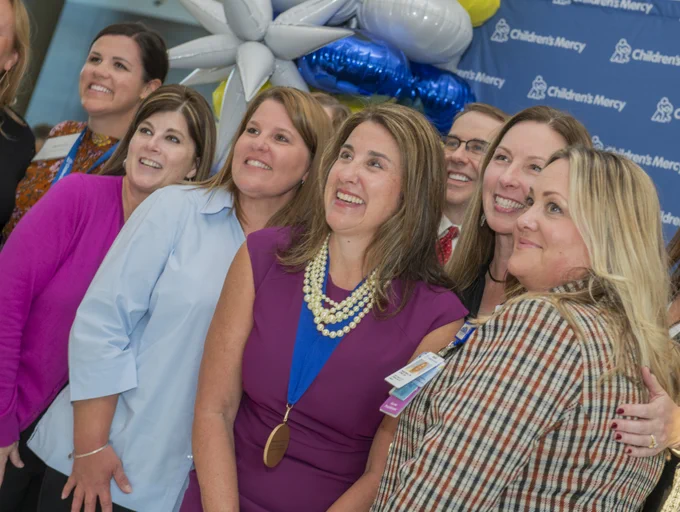 Group of individuals smiling at a Children's Mercy event, standing in front of decorative balloons.