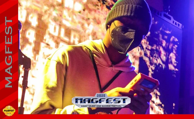 A photo of chiptune composer amateurLSDJ is displayed. He can be seen masked and donning warm attire, focused on a Gameboy in his hands as he performs a live set.