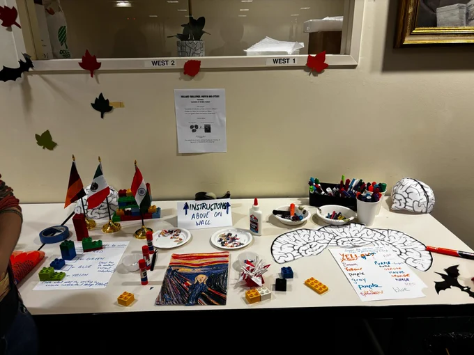 Picture of the science/art game attendees could play. On a table there are flags, legos, markers, glue, brain cut-outs and a picture of Edvard Munch's painting "The Scream".