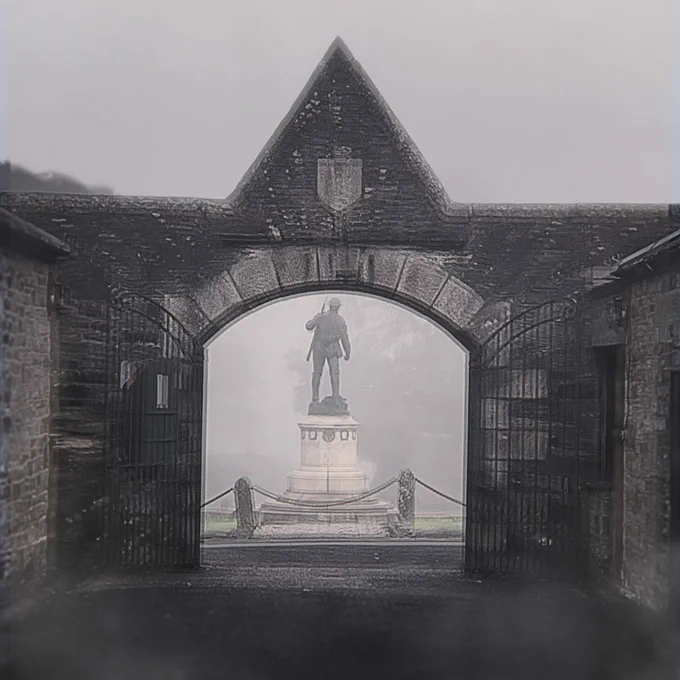 Against a very foggy background, the entrance to Bodmin Keep is very black and blurry. Through the archway the First World War memorial of a soldier can be seen, standing on a marble plinth and turned away from the viewer. 