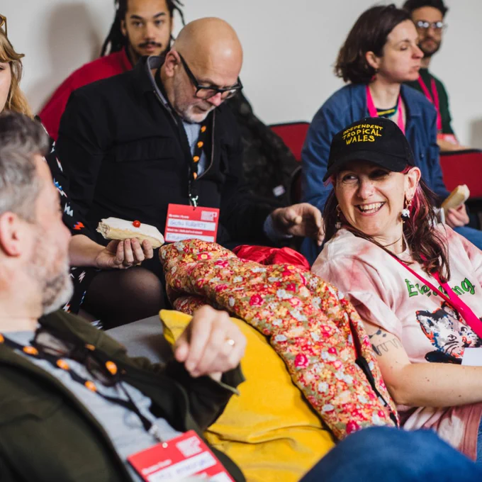 two people sitting on red chairs in an audience setting, they are looking at each other talking and smiling