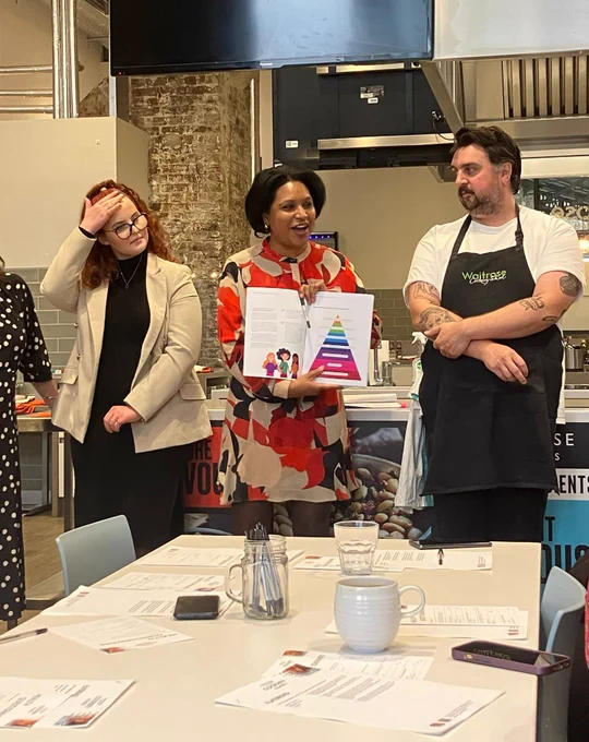 Photo of Janet Daby MP speaking with representatives from the Care Experienced Advisory Board and from the Waitrose Cookery School. She is holding open the new Higher Education Handbook.