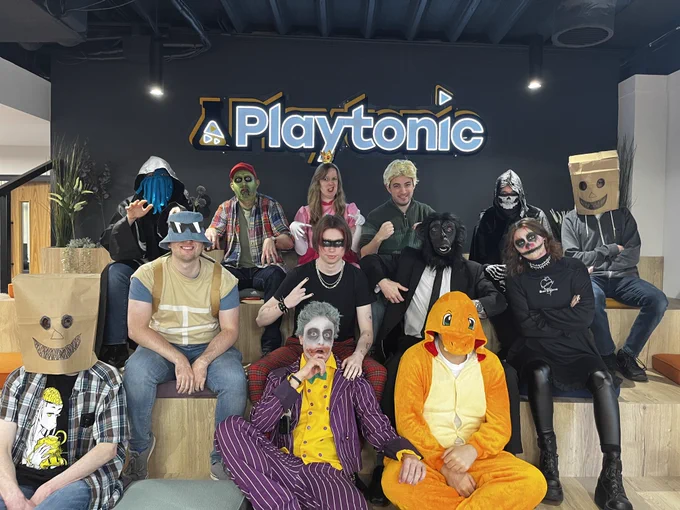 Photo of some of the Playtonic team sat on "the bleachers" with people in a variety of halloween costumes including: A cthulu looking guy, cool Squirtle from the Squirtle Squad, Charmander, the Joker, a zombie, a monkey is a suit, Princess Peach, a cool punk guy!