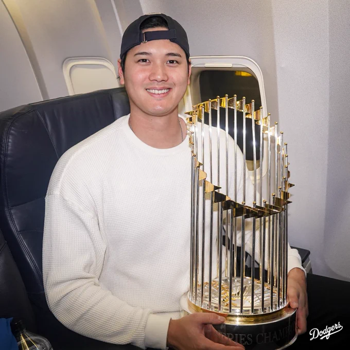 Shohei Ohtani smiles while holding the World Series trophy on the plane.
