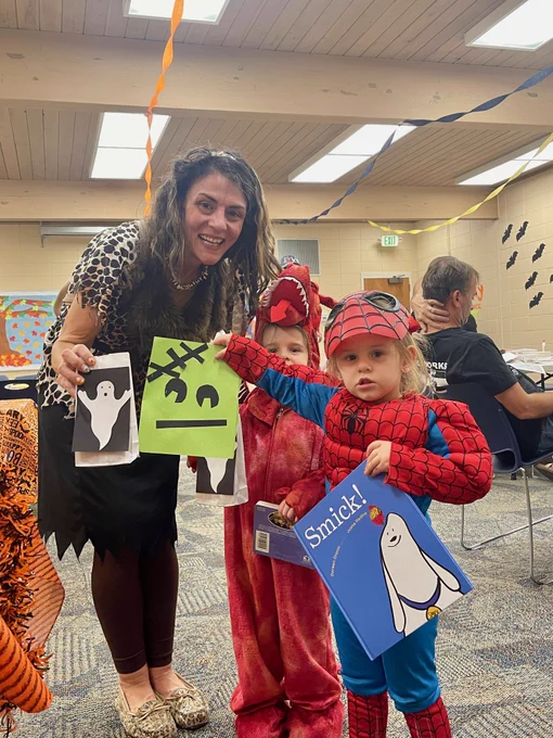 An adult and two kids dressed as spider-man and a dragon holding up their Frankenstein and Ghost crafts