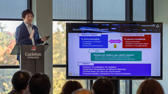Professor from Osaka University presenting next to a TV screen.