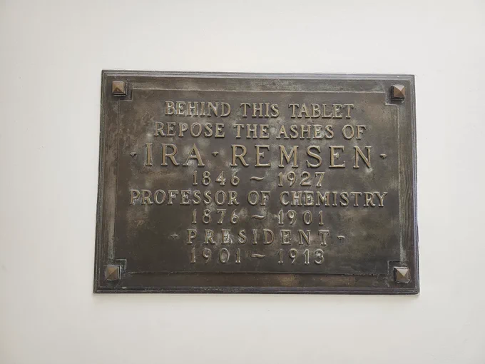 A bronze plaque embedded on a wall that read “behind this tablet repose the ashes of Ira Remsen 1846 – 1927 Professor of Chemistry 1876 – 1901 President 1901 – 1913”. 