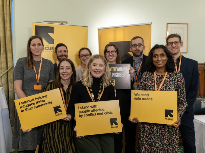 IRC staff in Parliament holding up signs that read: "I support helping refugees to thrive in their community," "I stand with people affected by conflict and crisis" and "We need safe routes".