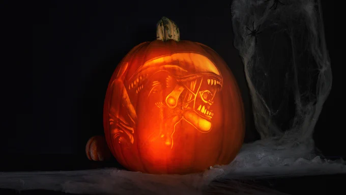 A glowing pumpkin with the xenomorph from Alien: Isolation intricately carved into it. Cobwebs surround the pumpkin, with spiders crawling over them.