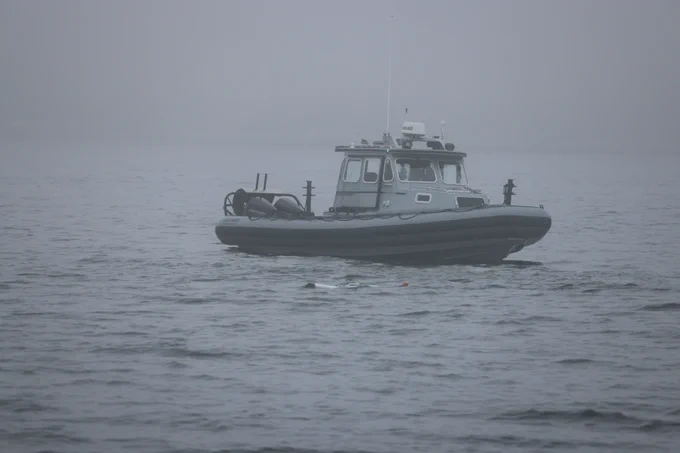 A boat on the water. The sky appears misty, water is slightly rough. There is a small piece of an underwater glider at the surface of the water, peeking out.
