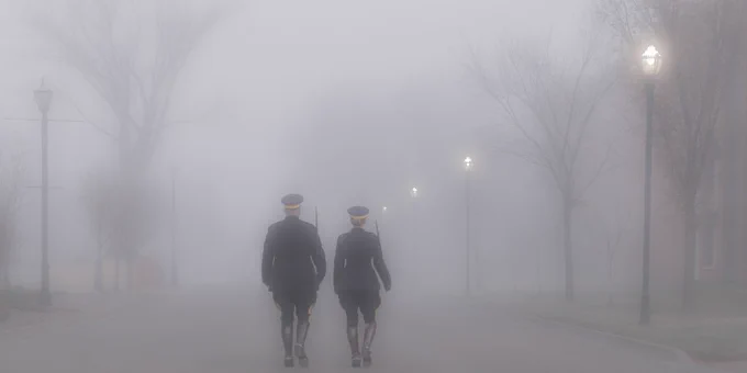 Two members in uniform walk down the street. There is fog in the background.
