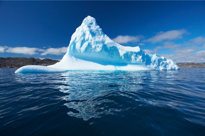 An iceberg floats in a bright blue sea.