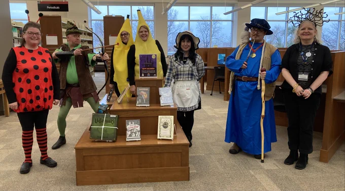 Photo of costumed staff members standing next to a library book display with horror materials.