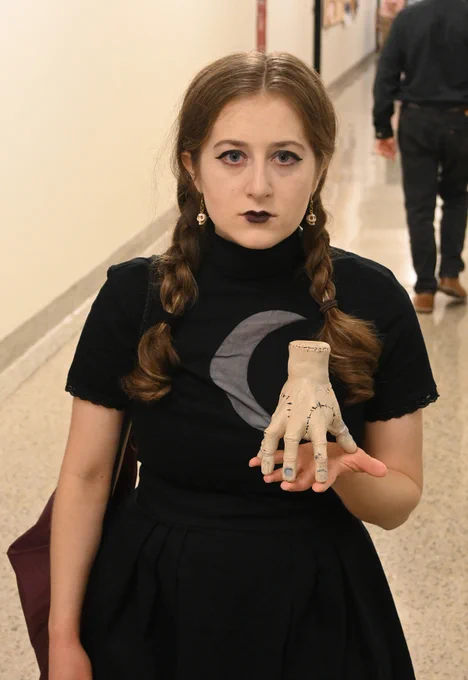 Student dressed as Wednesday from the Addam family tv show and movie holding Thing  in her hand.