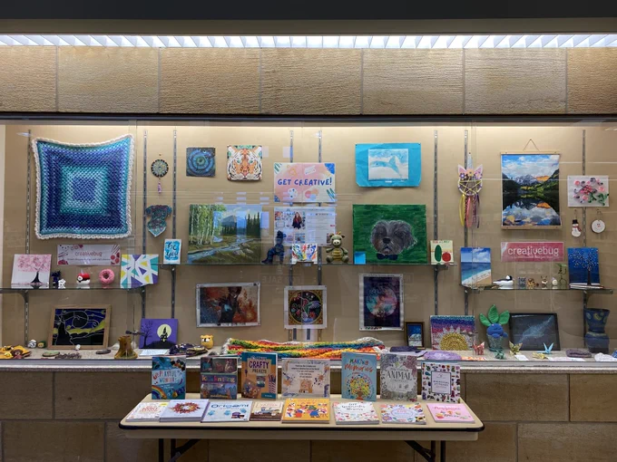 Large display case set into the wall filled with paintings, fiber crafts, paper craft, and more