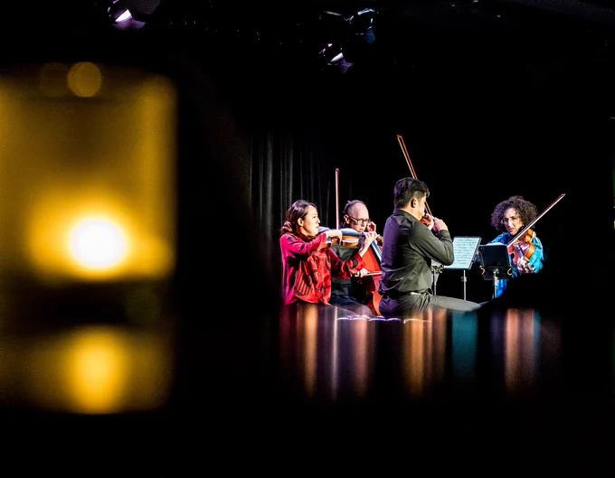 The Verona Quartet playing string instruments on a dimly lit stage, with a soft focus candle light in the foreground.