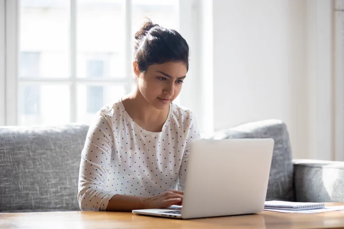 A person sitting on a couch and using a laptop on a coffee table. 