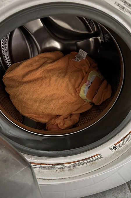 A crumpled garfield costume is looking out from the inside of a washing machine.