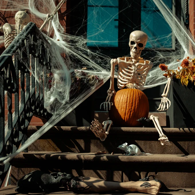 A cobwebbed skeleton sits on a stoop with a pumpkin