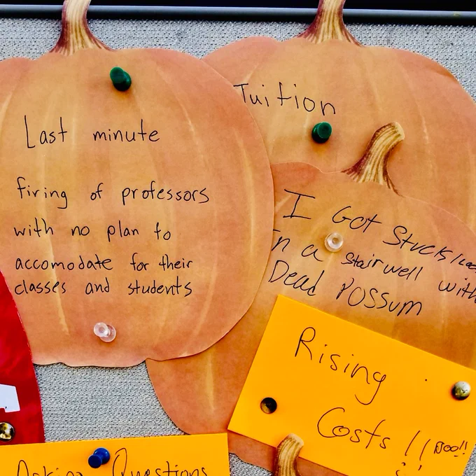 [Image description: a photograph shows orange and pumpkin-shaped notes featuring handwritten notes reflecting the fears and spooky experiences of various members of the Queens College community. Examples include “last-minute firing of professors with no plan to accomodate for their classes and students,” “rising costs,” and “I got stuck/locked in a stairwell with a dead possum”]