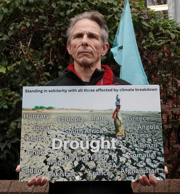 Man holding a photo of scorched earth titled Drought superimposed with the names of 20 countries recently effected. 