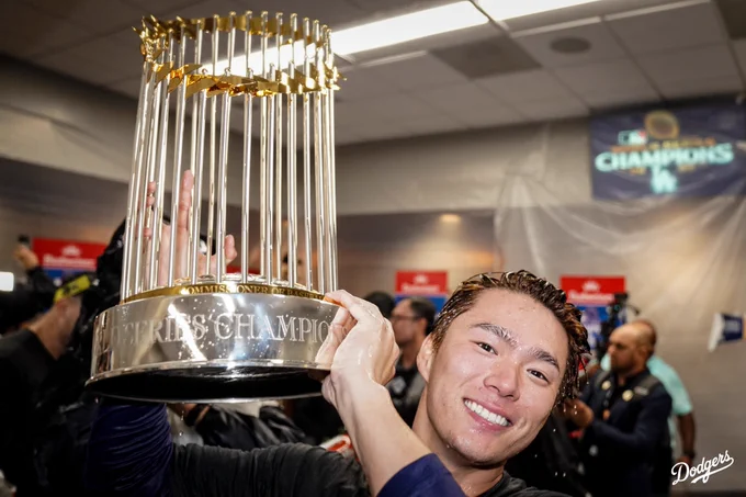 Yoshinobu Yamamoto smiles and holds up the World Series trophy.