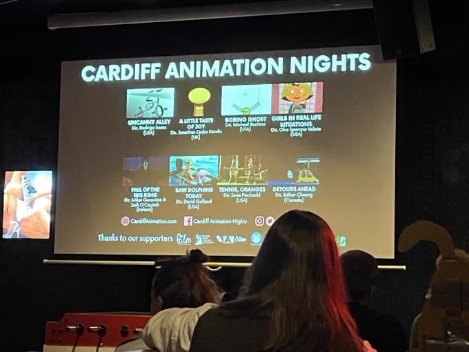 A pop-up cinema screen with people sitting in front of it. Large text on the screen reads “Cardiff Animation Nights” and there are thumbnails of animated films underneath. 
