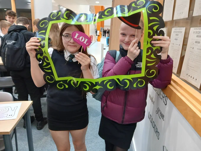 Two pupils holding up silly props, one with a top hat and the other with a sign that says LOL!