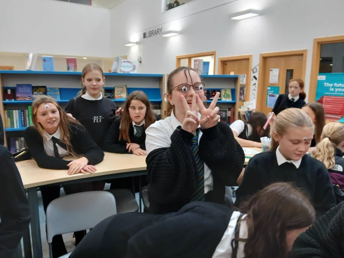 Pupils in s group in school library, with one pupil wearing glasses with fake stick on eyes