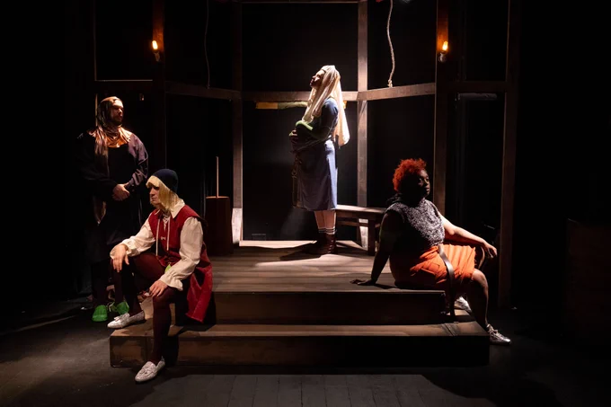A scene on stage from Beards. Four people in medival dress stand on a darkened stage. 
