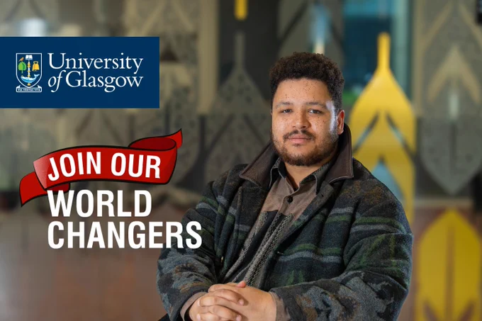 Image shows JMS Scholar Aaron Pocock leaning to one side with their fingers interlocked, wearing a buttoned shirt and winter coat.