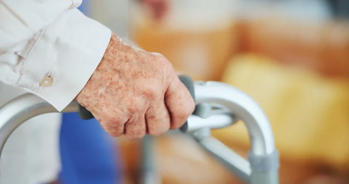Hand, senior person and walking frame with balance, recovery and mobility exercise in house. Elderly patient, steps and rehabilitation for injury, stroke or osteoporosis.