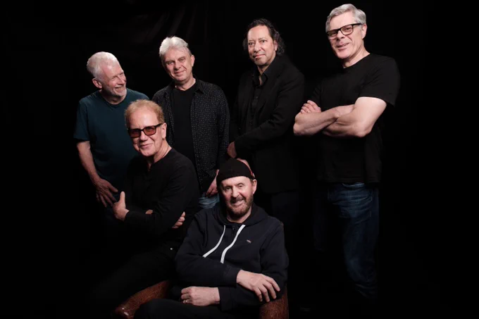 The six members of Oysterband wearing black on the top against a plain black background.