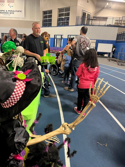 People waiting in line along the Turnstone fieldhouse track. The track is lined with booths handing out candy to kids dressed up for Halloween. 
