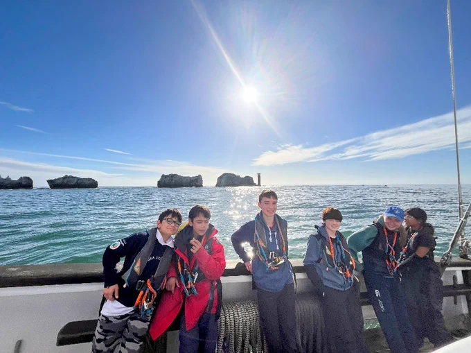 Crew on deck with the Needles and sunshine behind them