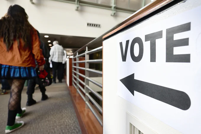 People walking in a hallway with a "VOTE" sign pointing left.
