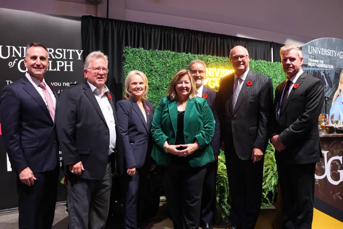 A group of people in suits smile for a photo in front of several University of Guelph signs.
