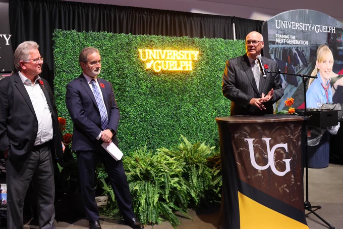Minister Rob Flack speaks at a podium as Senator Rob Black and University of Guelph Acting President, Rene Van Acker, listen to his remarks.