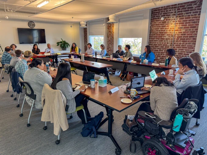 A view of the fellows training room from the back, with a round-table style setup and panelists on the far end.