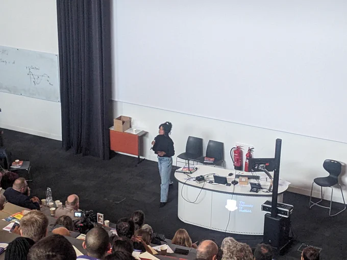 A woman with a microphone speaking to an audience in a lecture theatre
