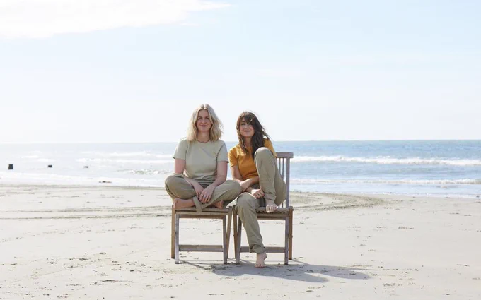 Lizzy and Catherine Ward Thomas sat next to each other on wooden garden chairs on a beach.