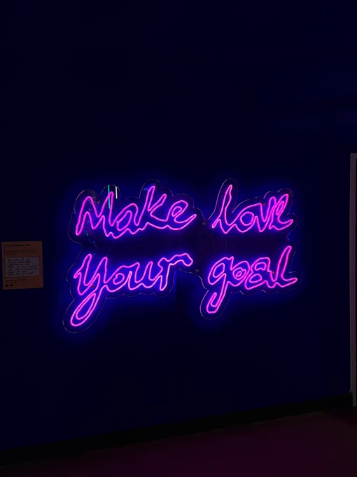 A neon sign that says Make Love Your Goal in pink