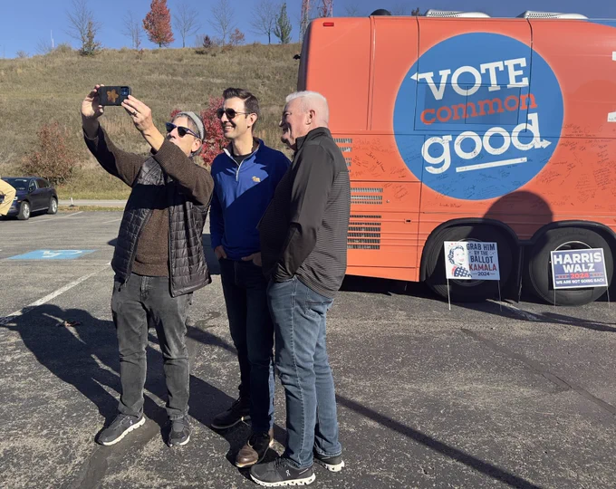 Chris Deluzio poses for a selfie with two men. Behind them is the back of a tour bus with the text “vote common good.”
