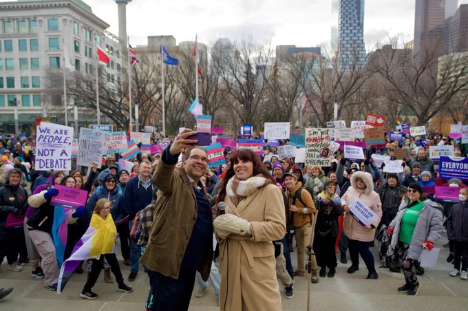 Naheed Nenshi and Dr. Victoria Bucholtz take a selfie with a thousand supporters at trans rights rally