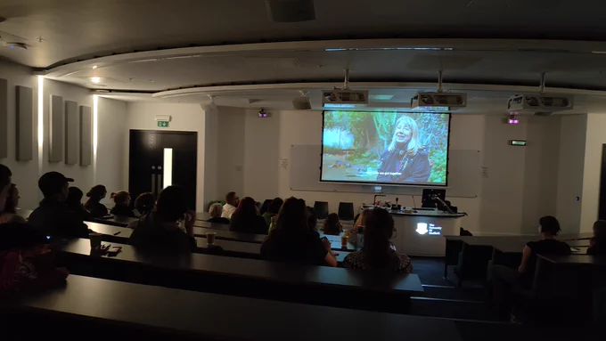 A photo of a group of people in a lecture theatre watching a film on a screen