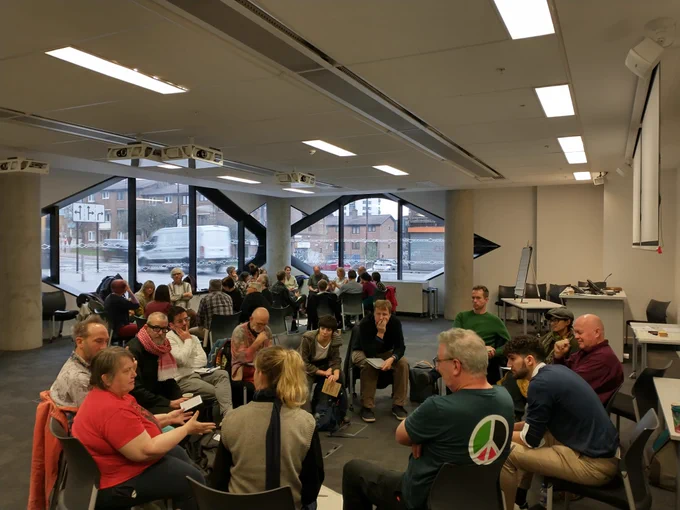 A photo of a large brightly lit room, with dozens of people sat in two circles discussing things