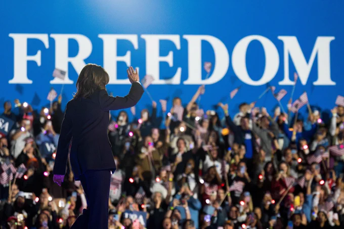 Kamala Harris waving to a crowd at a rally with "FREEDOM" sign in the background.
